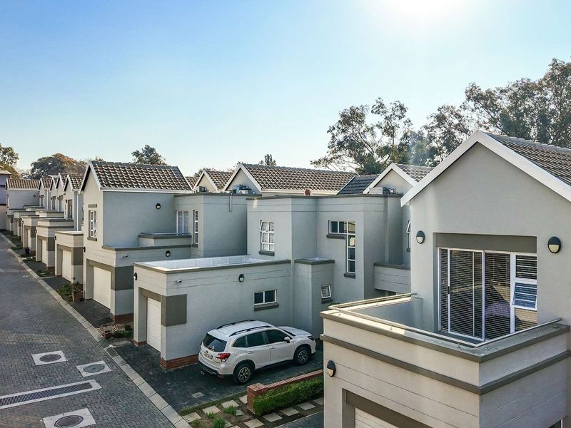 An elevated view of a modern cluster housing complex featuring paved driveways, tiled roofs, and attached garages with balconies.