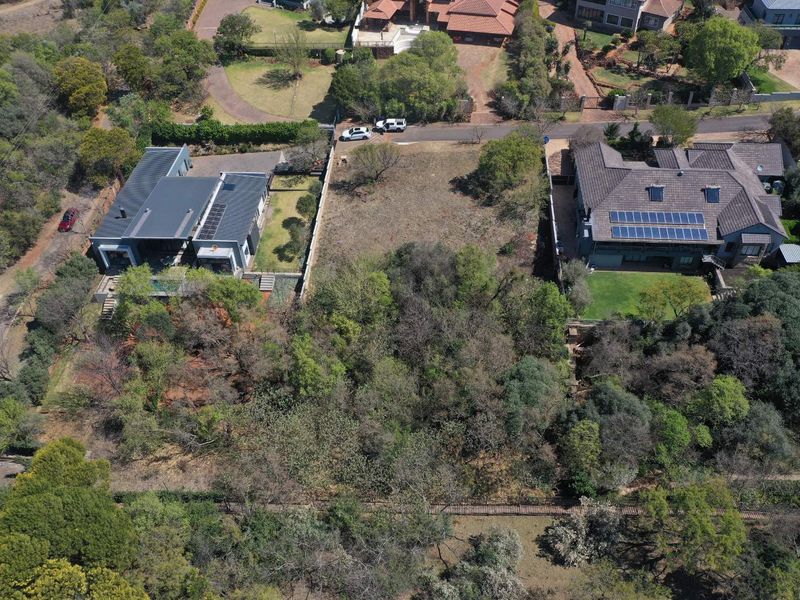 An aerial view of a vacant residential plot situated between two existing properties, featuring established trees and natural vegetation.