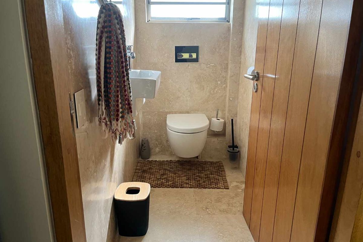 A compact guest bathroom featuring natural stone wall and floor tiles, a wall-mounted toilet, and a small wall-hung basin.