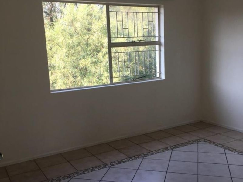An empty bedroom featuring tiled flooring with a decorative border and a window fitted with security bars.