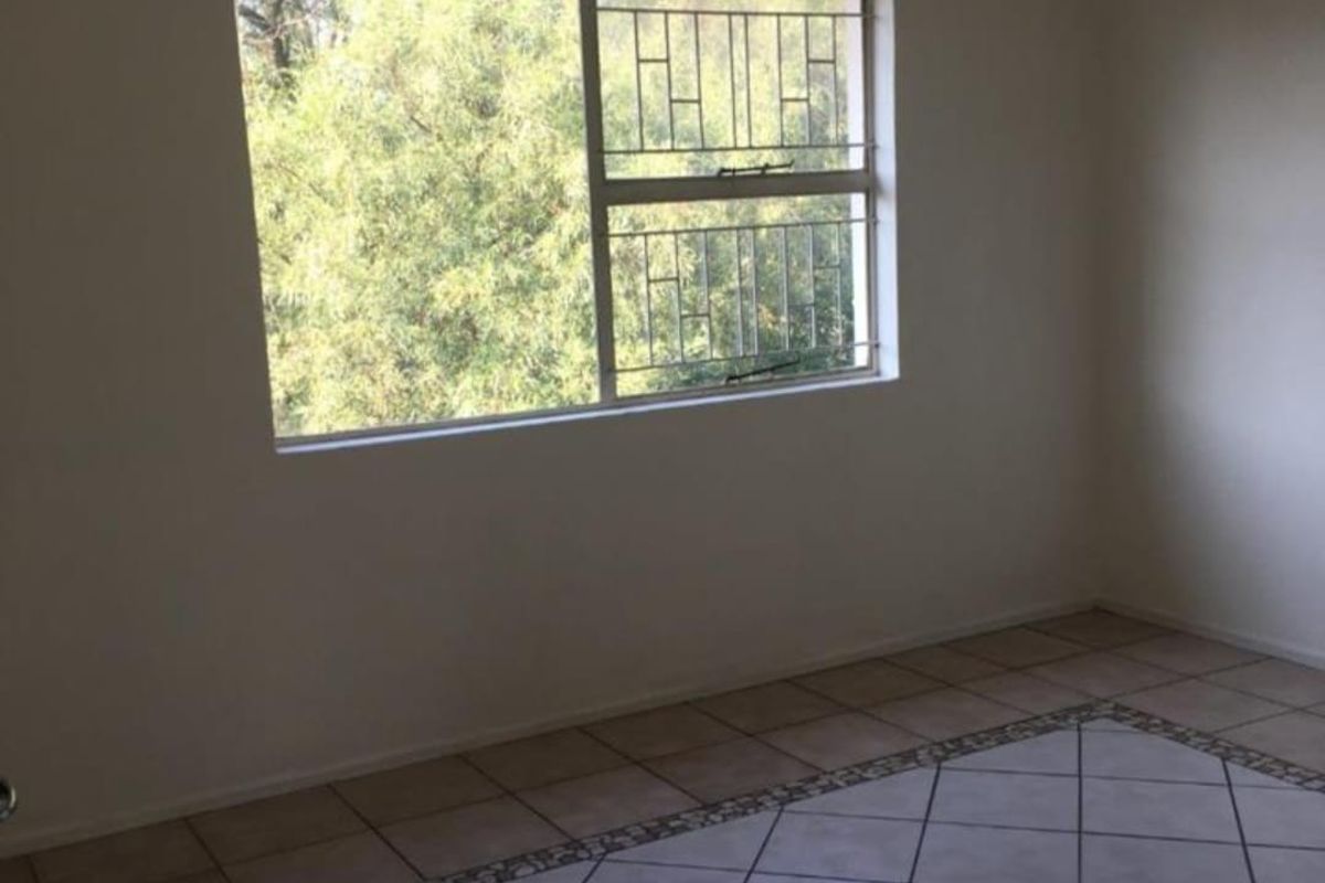An empty bedroom featuring tiled flooring with a decorative border and a window fitted with security bars.