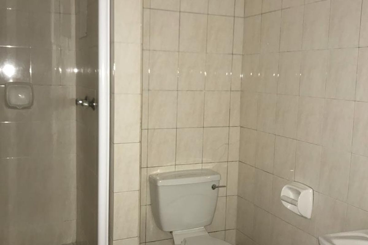 A functional bathroom featuring a shower enclosure, toilet, and wash basin with neutral wall and floor tiling.