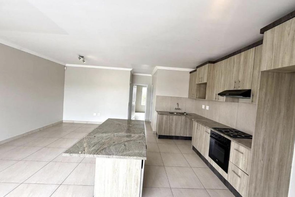Spacious open-plan kitchen and living area featuring a granite island, built-in oven, hob, extractor fan, and modern cabinetry with neutral tiled flooring.