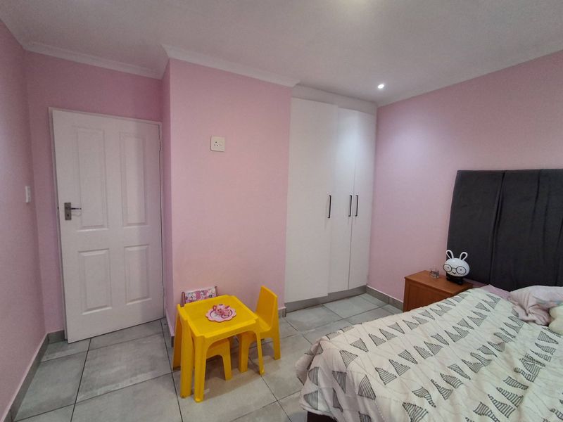 A well-maintained bedroom featuring neutral tiled flooring, built-in white cabinetry, and recessed lighting, providing a clean and functional living space.