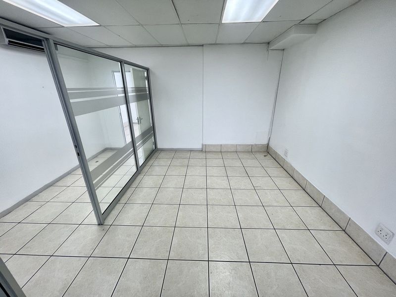 A vacant office space featuring ceramic tiled flooring, a glass partition wall, suspended ceiling with integrated lighting, and an installed air conditioning unit.