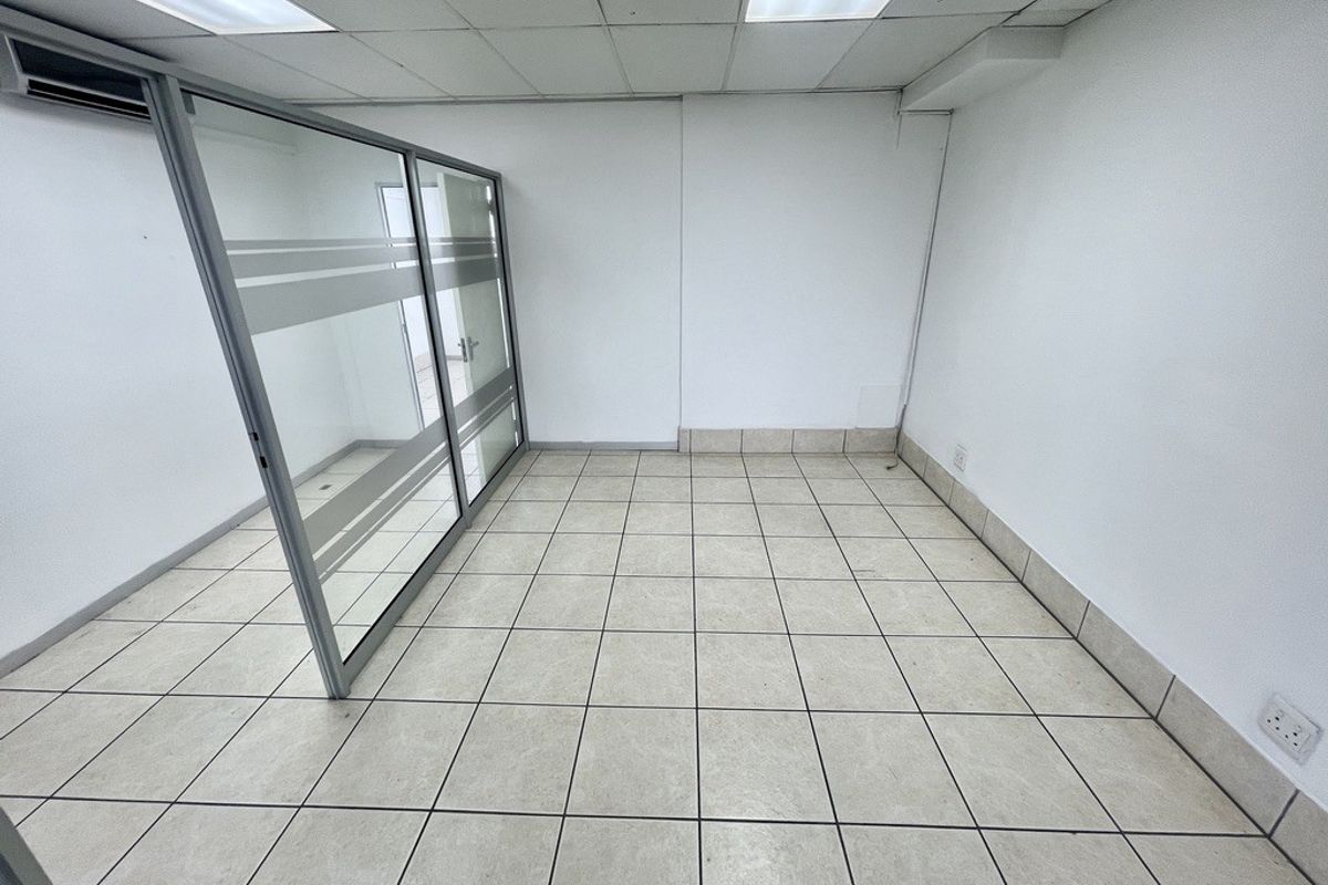 A vacant office space featuring ceramic tiled flooring, a glass partition wall, suspended ceiling with integrated lighting, and an installed air conditioning unit.