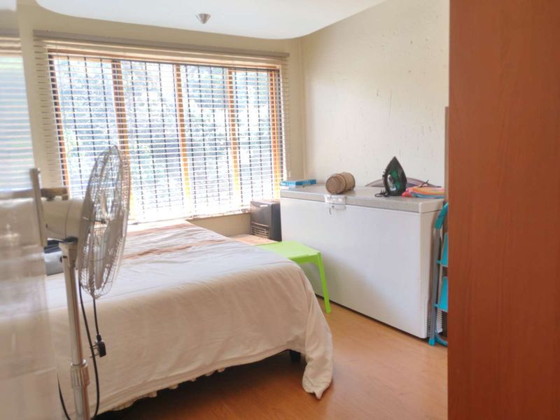 A bedroom featuring laminate flooring and venetian blinds, showing signs of wear including visible wall plaster cracks.