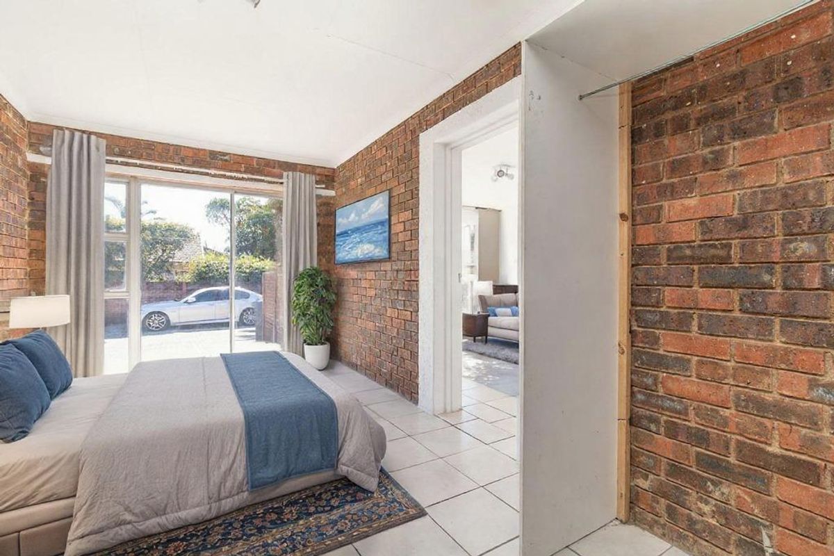 Bedroom featuring exposed brick walls, tiled flooring, and sliding glass doors providing access to the exterior.