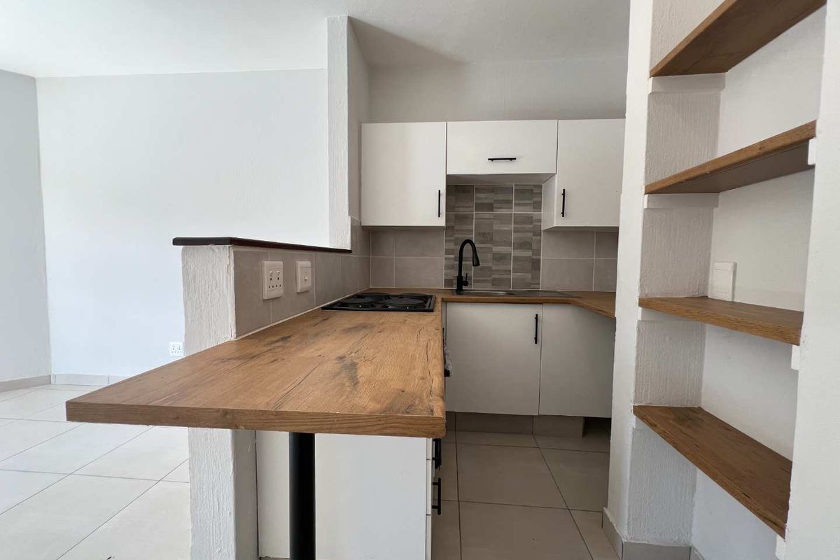 Modern kitchen featuring white cabinetry, wood-look countertops, a built-in hob, and integrated shelving, creating a functional and stylish open-plan cooking space.