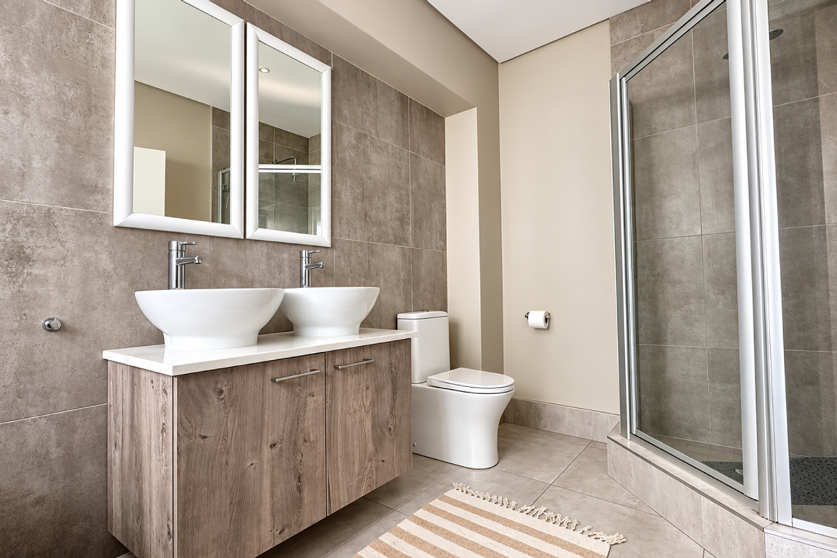 Modern bathroom featuring a double vanity with vessel sinks, wall-mounted mirrors, a toilet, and a glass-enclosed shower with neutral tiled finishes.