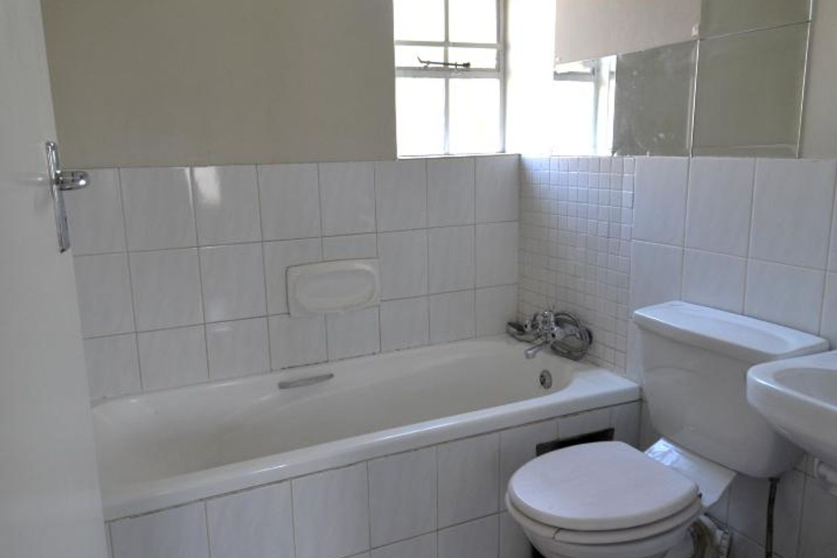 A functional bathroom featuring a bathtub, toilet, and washbasin with tiled finishes. The space requires cosmetic updates to address wall damage and dated fixtures.