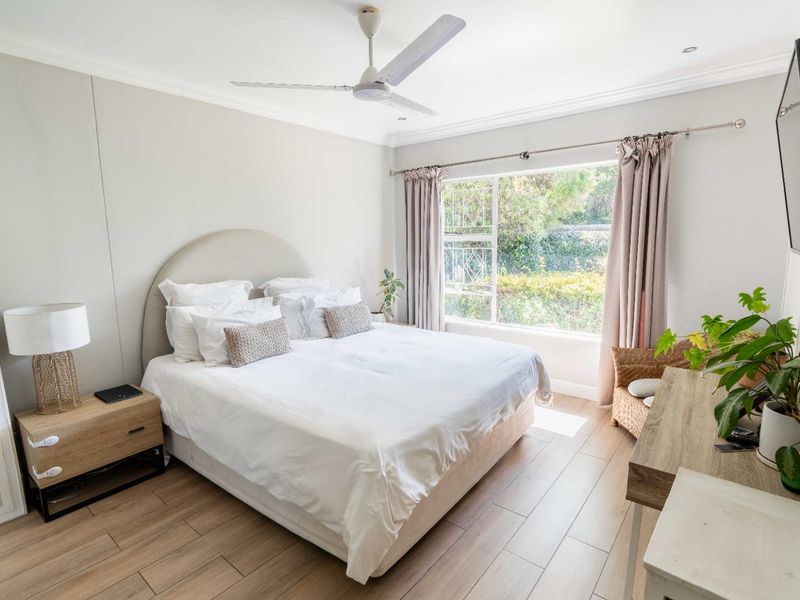 A bright and well-maintained bedroom featuring laminate flooring, a ceiling fan, and a large window overlooking the garden.