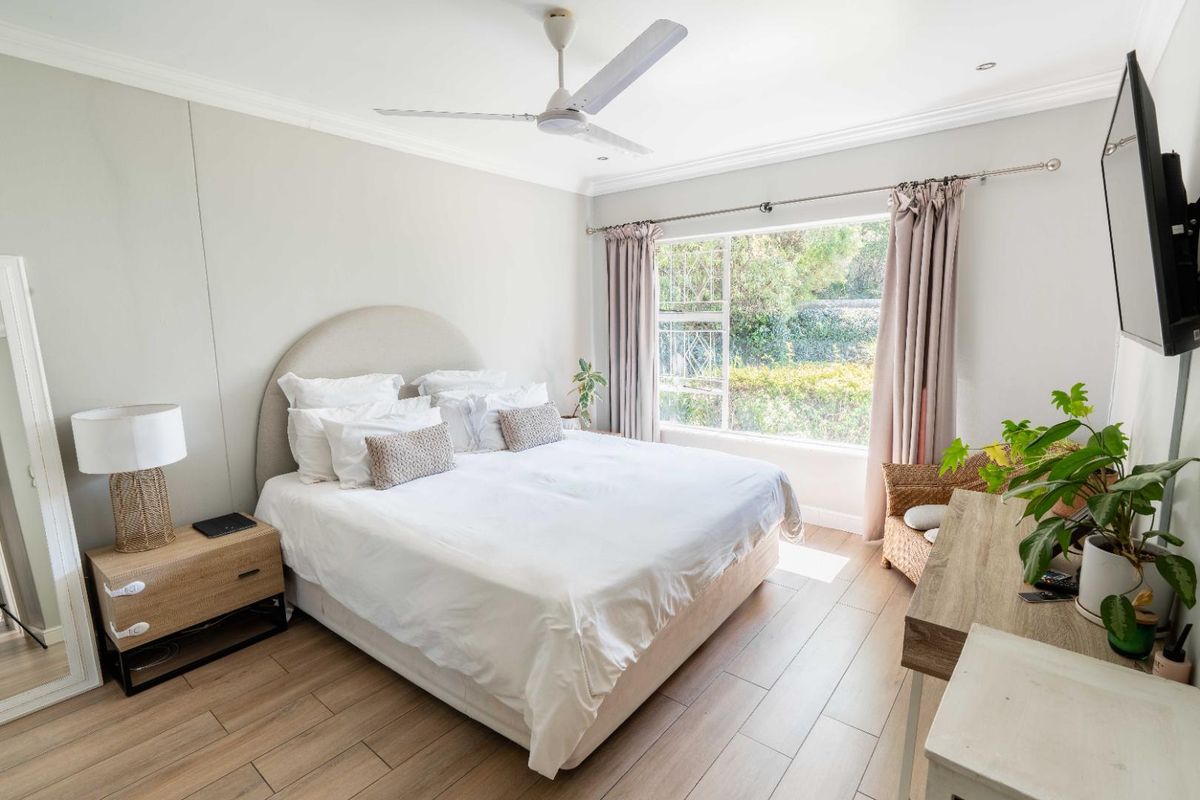 A bright and well-maintained bedroom featuring laminate flooring, a ceiling fan, and a large window overlooking the garden.