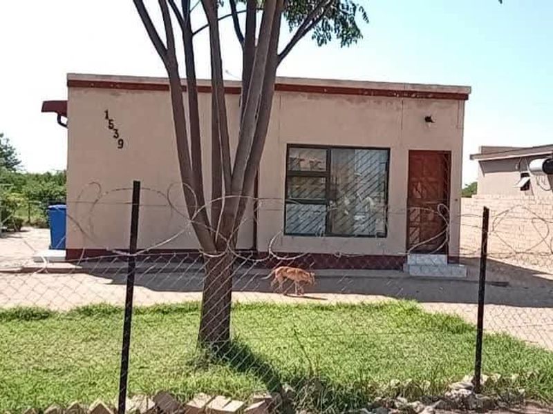 Front view of a single-story residential property featuring a paved driveway, lawn area, and secure perimeter fencing with razor wire.