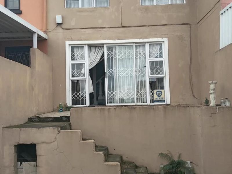 Rear elevation of the apartment featuring a sliding glass door with security gate, concrete staircase, and weathered exterior finishes.