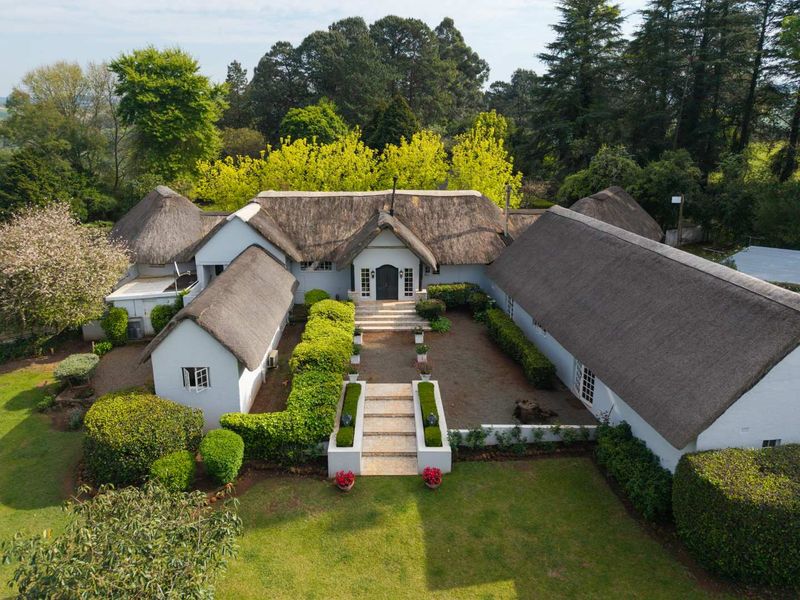 Aerial view of a charming farmhouse featuring a traditional thatched roof, a central courtyard with stone steps, and well-maintained landscaped gardens.