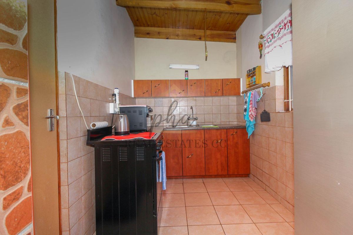 A compact kitchen featuring wooden cabinetry, tiled flooring, and a timber-clad ceiling, providing a functional prep area with basic built-in storage.