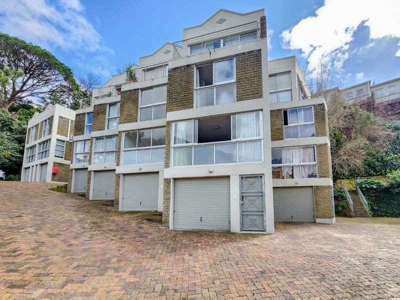 Front elevation of a multi-story apartment complex featuring multiple garage units, brick facade detailing, and private balconies with sliding glass doors.