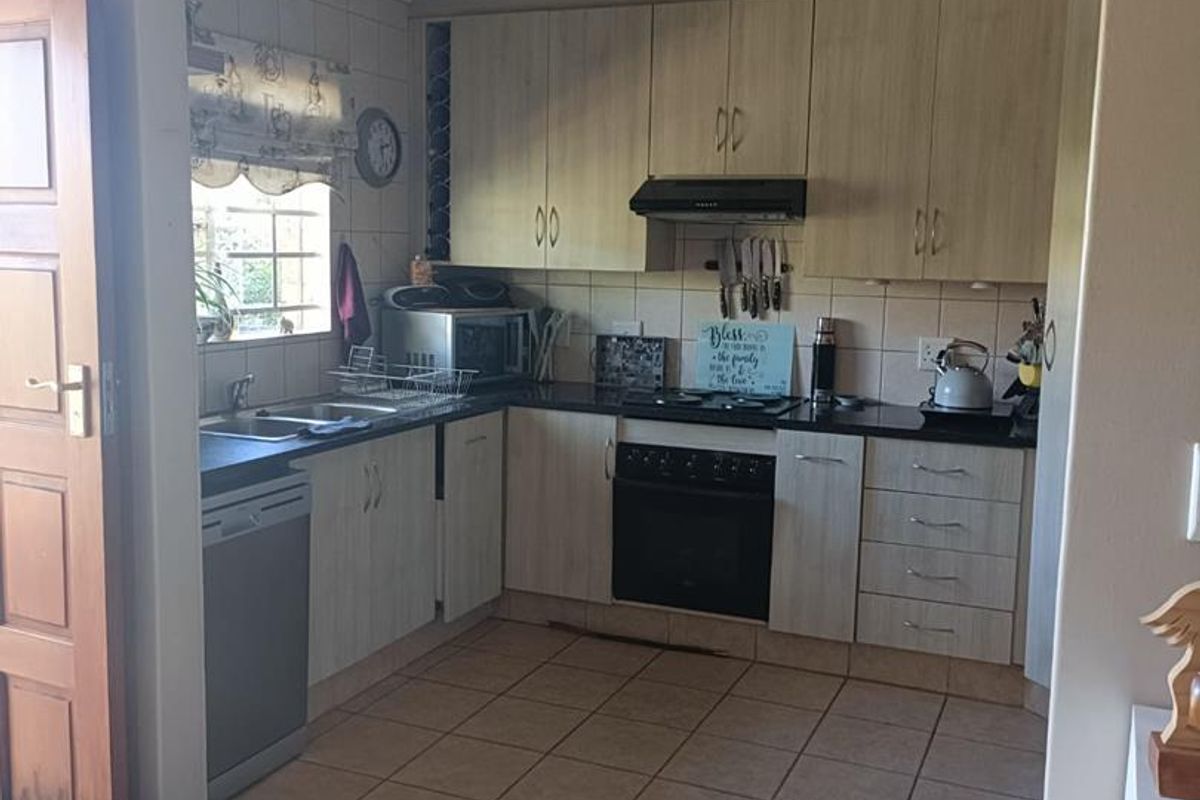 A functional kitchen featuring light-toned cabinetry, dark laminate countertops, built-in oven with hob, and tiled flooring, offering a practical layout for daily use.