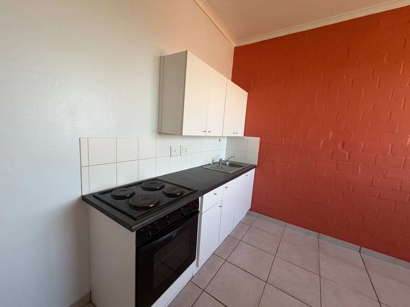 A compact kitchen featuring white cabinetry, a built-in electric stove and oven, stainless steel sink, and a distinctive orange brick feature wall.