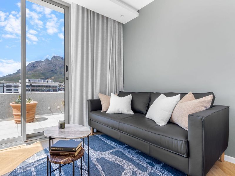 A modern living room featuring hardwood flooring, recessed lighting, and a large sliding glass door providing access to a balcony with mountain views.