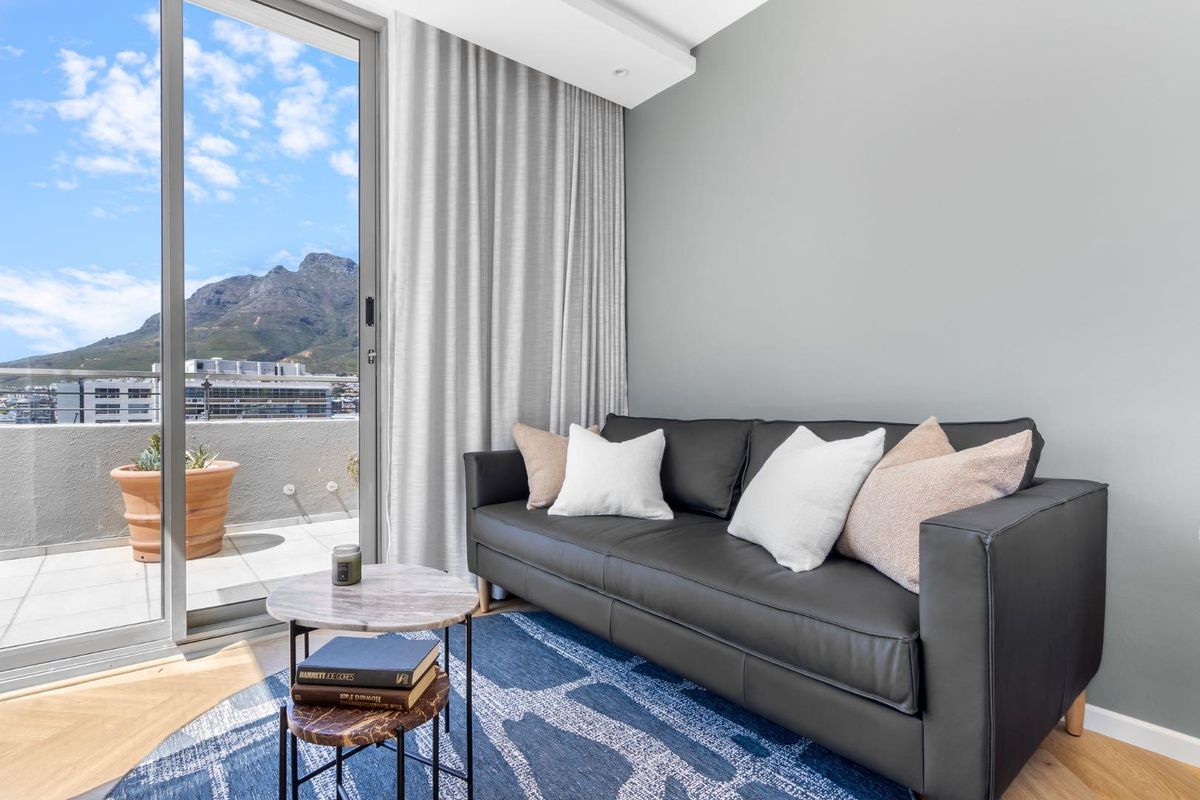 A modern living room featuring hardwood flooring, recessed lighting, and a large sliding glass door providing access to a balcony with mountain views.