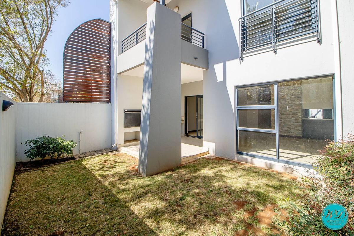 Rear view of the townhouse featuring a covered patio with a built-in braai, a small private garden, and an upper-level balcony.