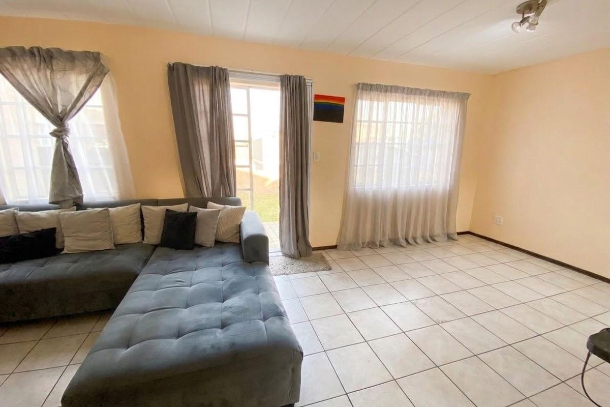 A bright living room featuring neutral tiled flooring, large windows for natural light, and direct access to the outdoor area through a sliding glass door.