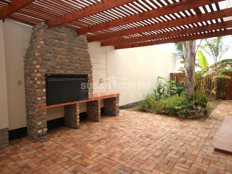 Covered outdoor patio featuring a built-in brick braai, timber pergola overhead, and durable brick paving, ideal for outdoor entertaining.