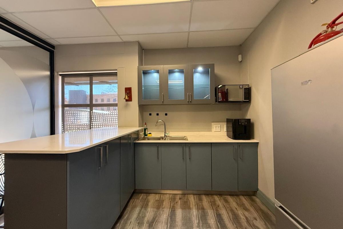 A modern office kitchenette featuring grey cabinetry, stone countertops, a stainless steel sink, and integrated lighting, providing a functional break area.