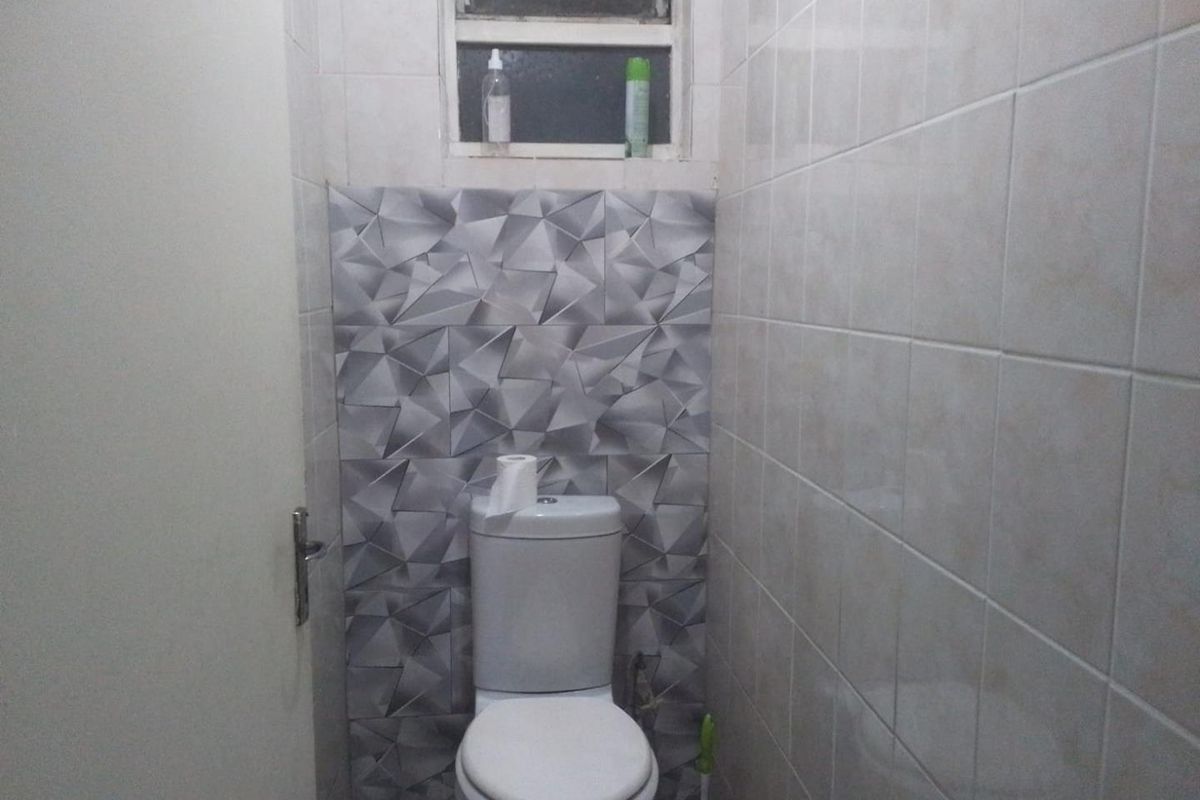 A compact bathroom featuring a standard toilet, tiled walls with a decorative accent section, and a small high-level window for ventilation.
