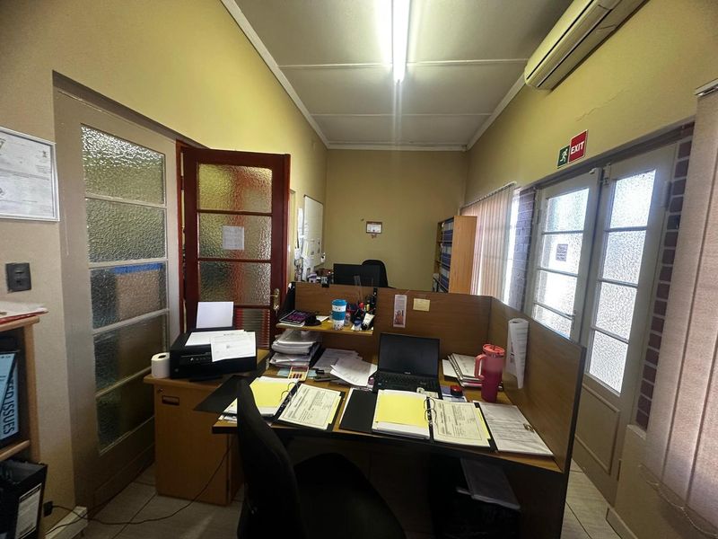 A functional office space featuring tiled flooring, timber-framed glass doors, and a wall-mounted air conditioning unit.