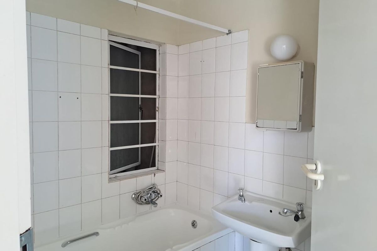 A dated bathroom featuring a white bathtub, pedestal basin, and tiled walls, requiring cosmetic updates to modernize the space.