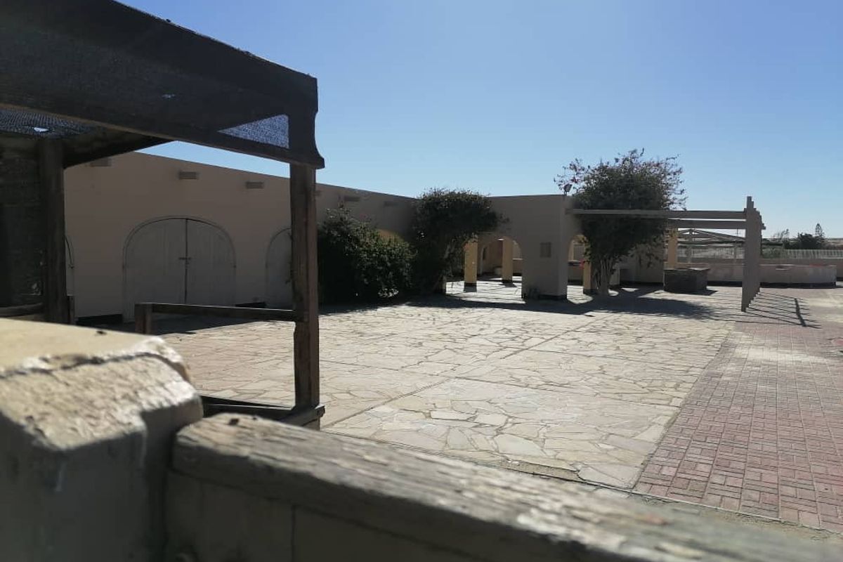 A spacious outdoor courtyard featuring stone paving, arched architectural details, and timber pergola structures, suitable for commercial or recreational use.