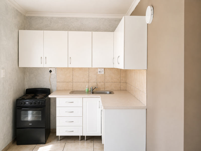 A compact kitchen featuring white cabinetry, a laminate countertop, tiled splashback, and a freestanding electric stove.