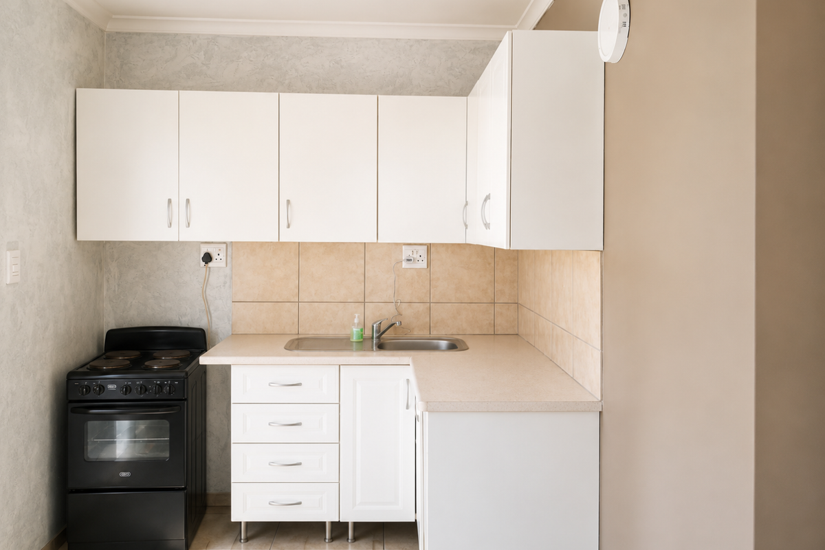 A compact kitchen featuring white cabinetry, a laminate countertop, tiled splashback, and a freestanding electric stove.