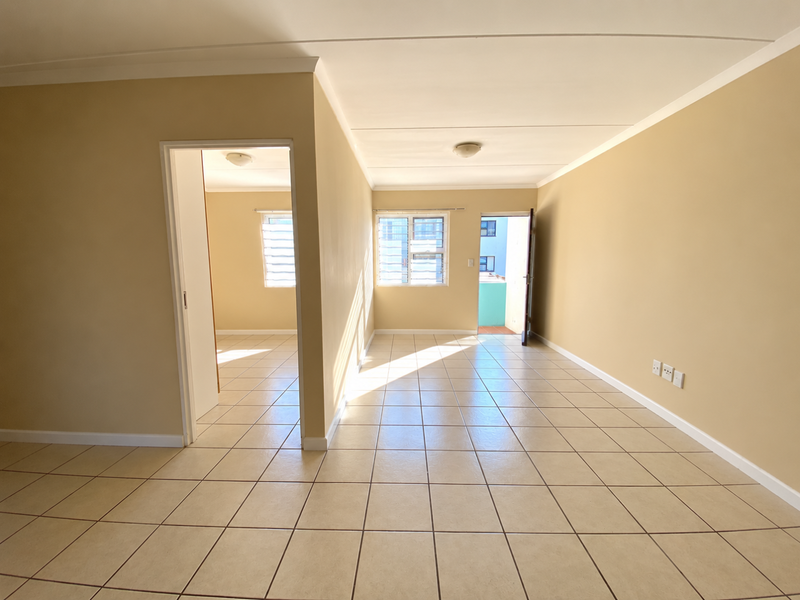 An empty, open-plan living area featuring neutral tiled flooring, louver windows, and direct access to an outdoor balcony space.