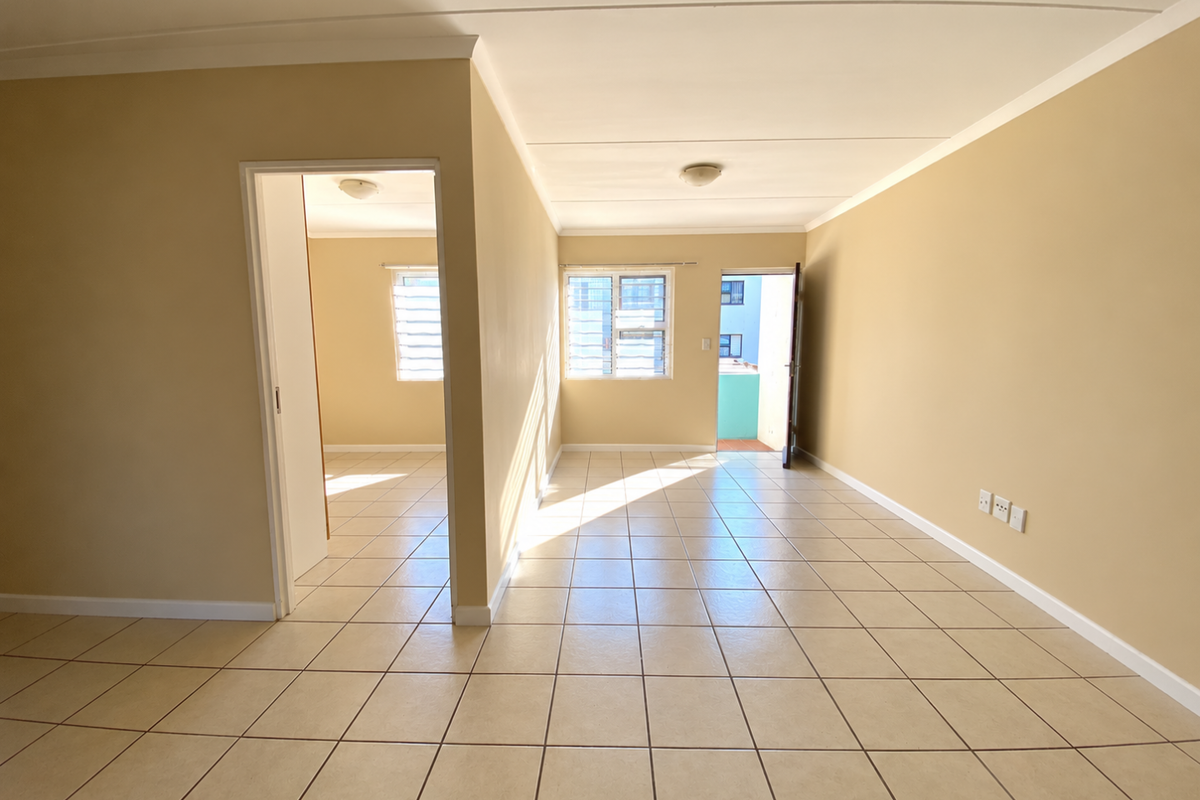 An empty, open-plan living area featuring neutral tiled flooring, louver windows, and direct access to an outdoor balcony space.