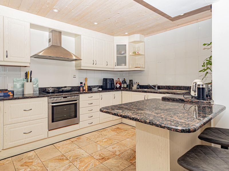 A functional kitchen featuring granite countertops, a built-in oven, stainless steel extractor fan, and a breakfast bar with timber ceiling finishes.