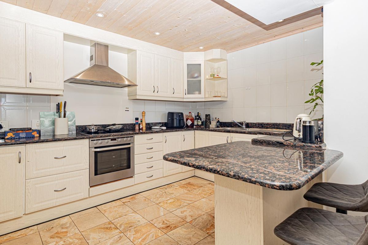 A functional kitchen featuring granite countertops, a built-in oven, stainless steel extractor fan, and a breakfast bar with timber ceiling finishes.