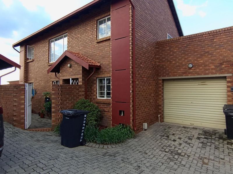 Front elevation of a face brick apartment unit featuring a paved driveway, integrated garage with a roller shutter door, and a covered entrance.