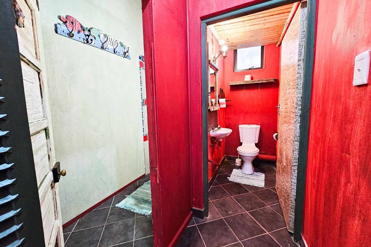 A compact bathroom featuring a wall-mounted basin, toilet, and tiled flooring, accessed via a hallway with bold red and green wall finishes.