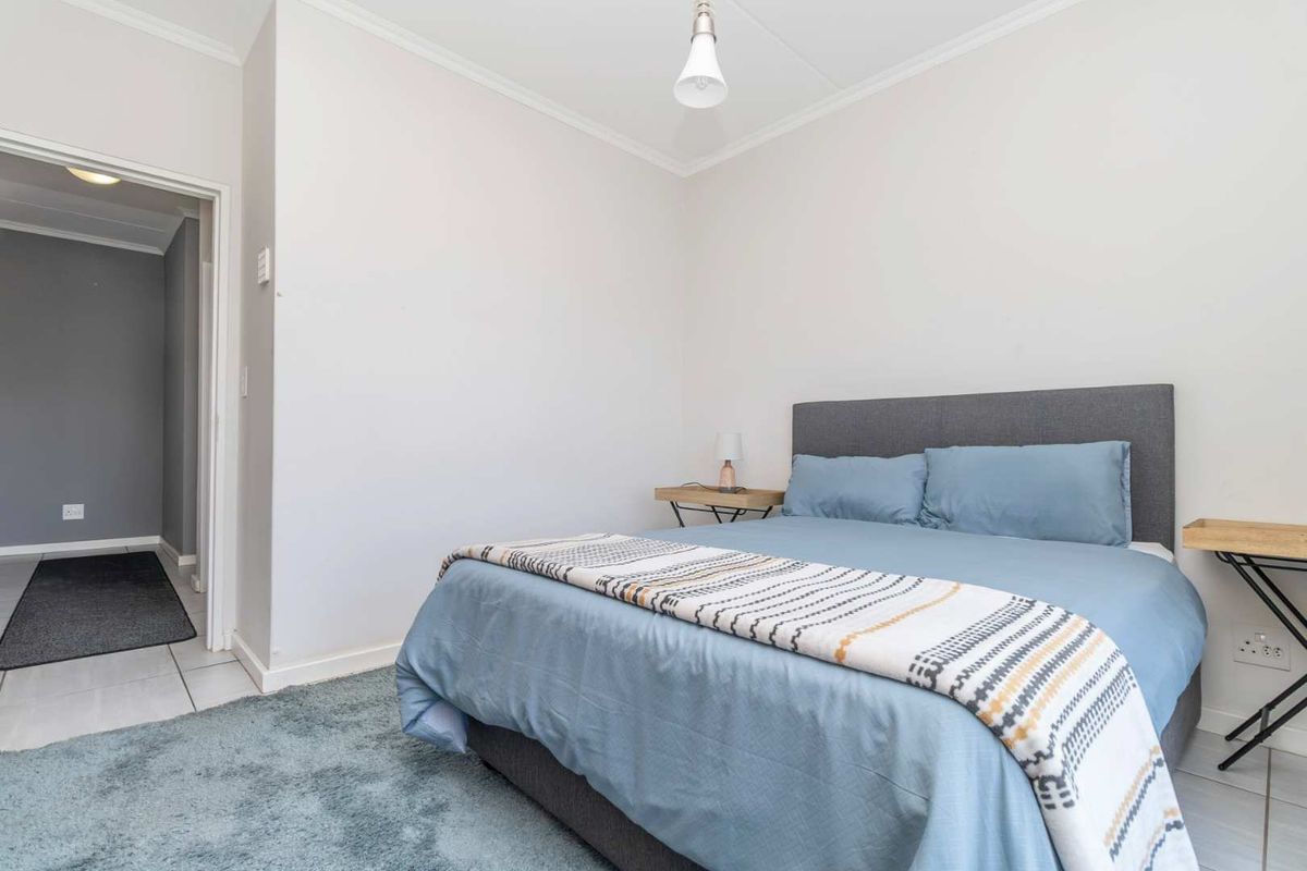 A well-maintained bedroom featuring neutral walls, tiled flooring, and a simple pendant light fixture, offering a clean and functional living space.