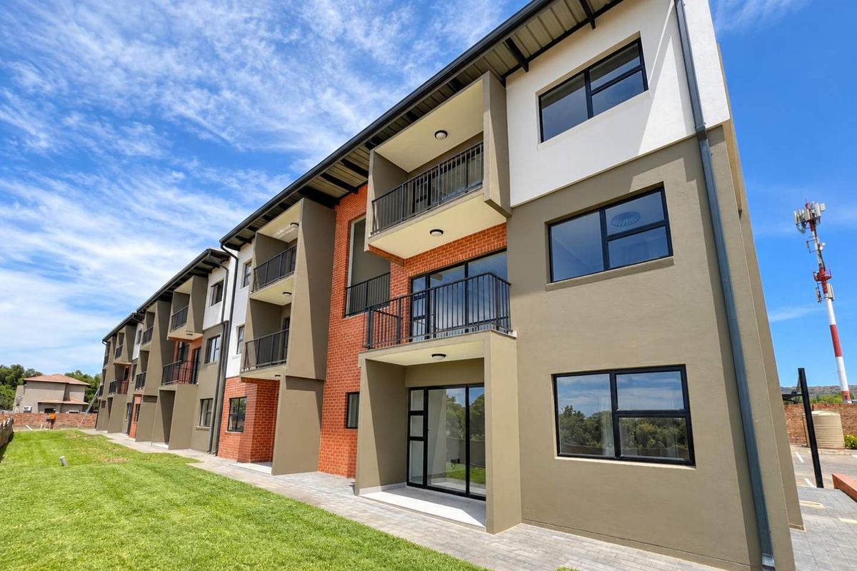A modern apartment building exterior featuring brick and painted plaster finishes, private balconies, and paved ground-level access with well-maintained lawn areas.