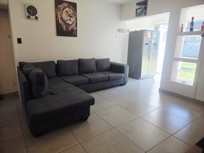 A living room area featuring neutral ceramic floor tiles, textured walls, and built-in display shelving, providing a functional and open living space.