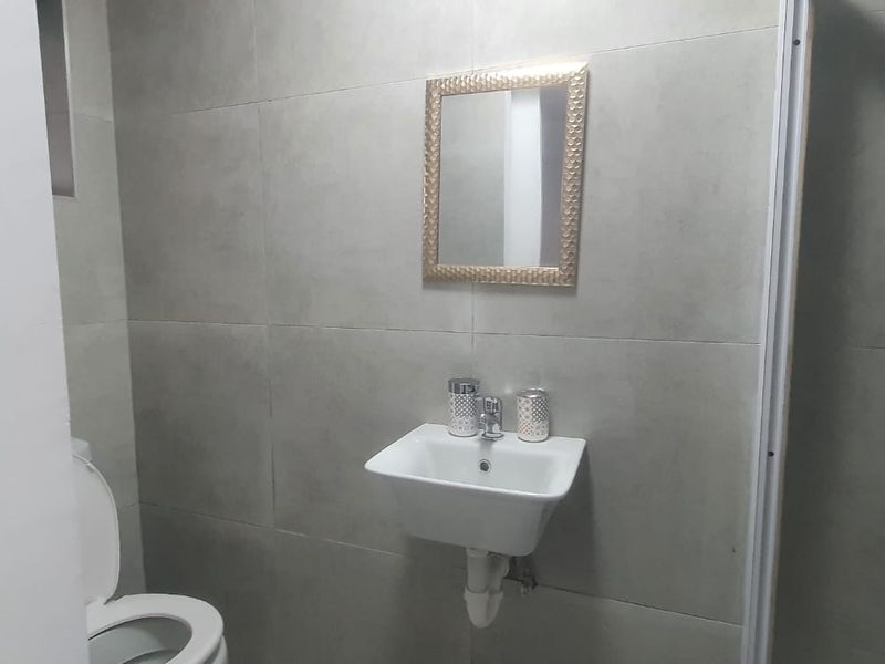 A compact bathroom featuring modern grey wall tiles, a wall-mounted basin, a toilet, and a shower enclosure.