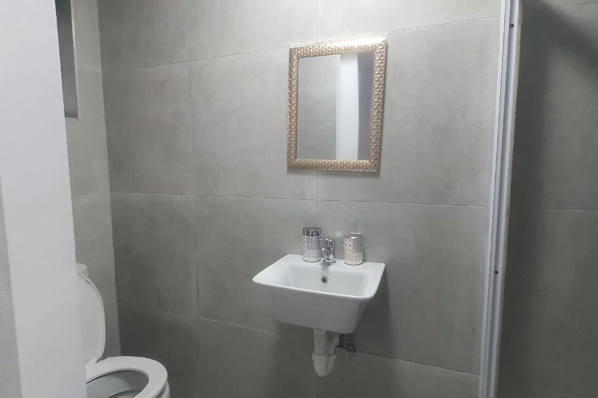 A compact bathroom featuring modern grey wall tiles, a wall-mounted basin, a toilet, and a shower enclosure.