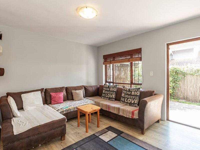 A comfortable living room featuring light-toned laminate flooring, a flush mount ceiling light, and direct access to the outdoor area through a glass door.