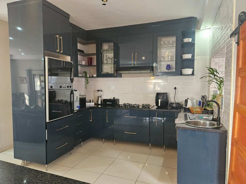 Modern kitchen featuring dark gloss cabinetry, granite countertops, built-in oven and microwave, gas hob with extractor, and tiled flooring.