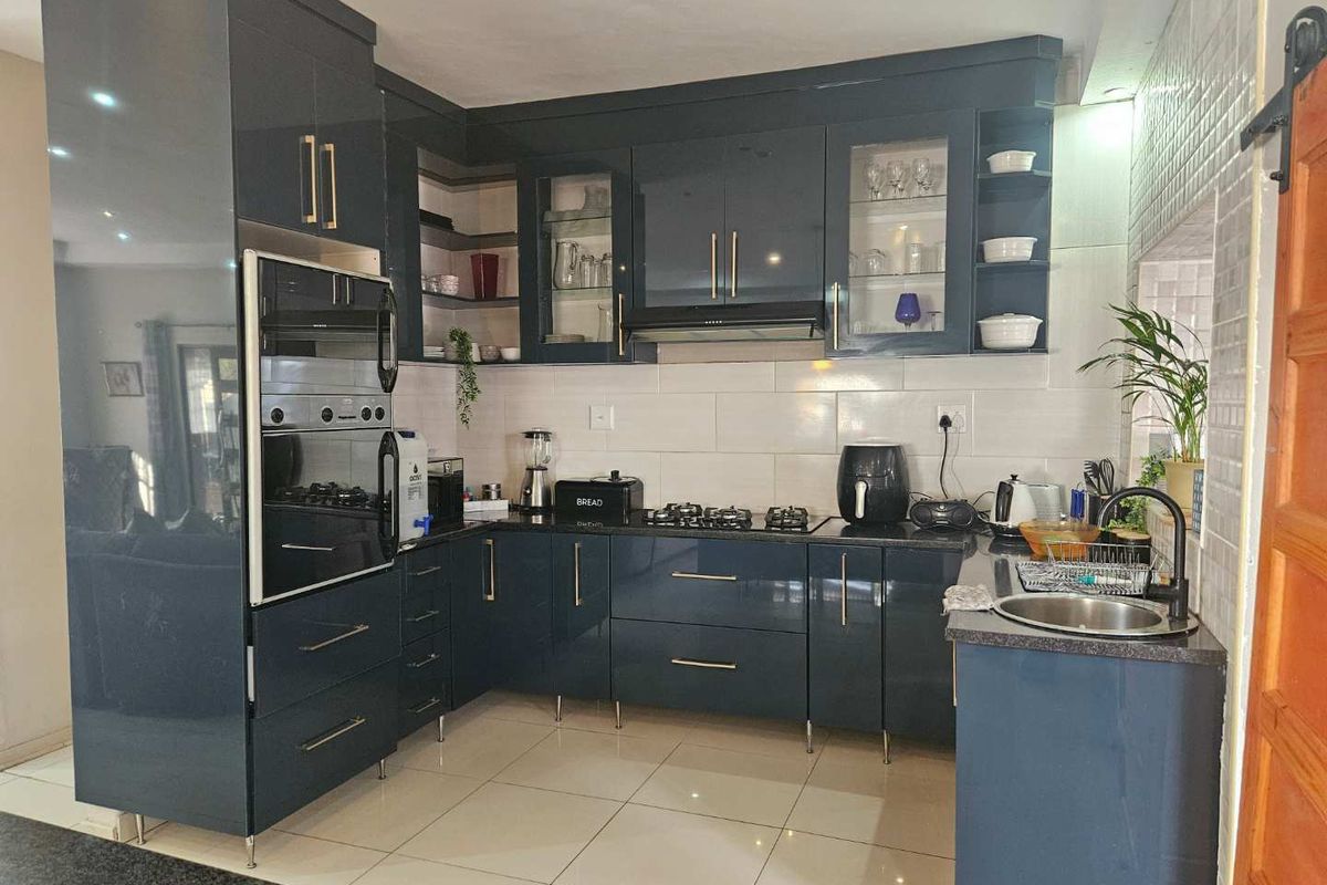 Modern kitchen featuring dark gloss cabinetry, granite countertops, built-in oven and microwave, gas hob with extractor, and tiled flooring.